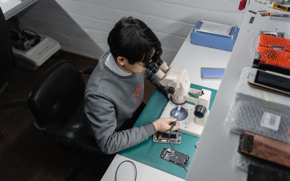 Technician repairing a smartphone under a microscope